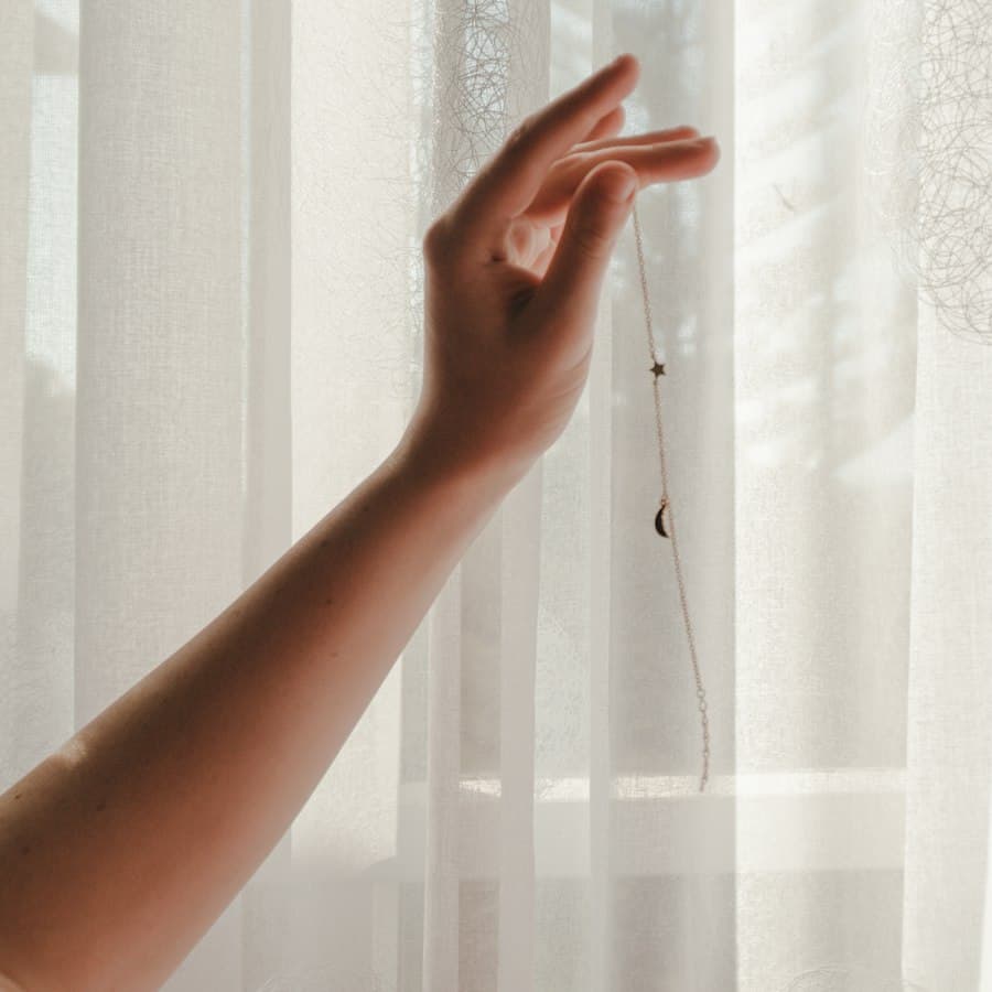 A hand holding back a curtain in daylight
